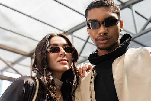 portrait of stylish interracial couple in trendy sunglasses looking at camera