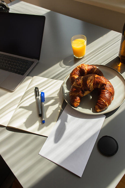 High angle view of croissants near laptop and orange juice on table at home