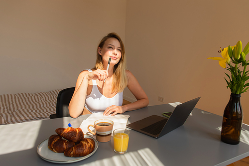 Pensive freelancer holding pen near breakfast and gadgets at home