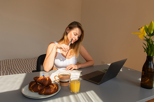 Freelancer in top looking at notebook near devices and breakfast at home