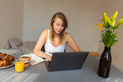 Blonde woman using laptop near breakfast and drinks at home