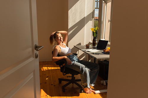 Happy barefoot freelancer looking at camera near devices and flowers at home