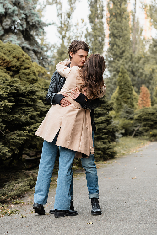 full length of young man dancing with brunette girlfriend in trench coat in autumnal park