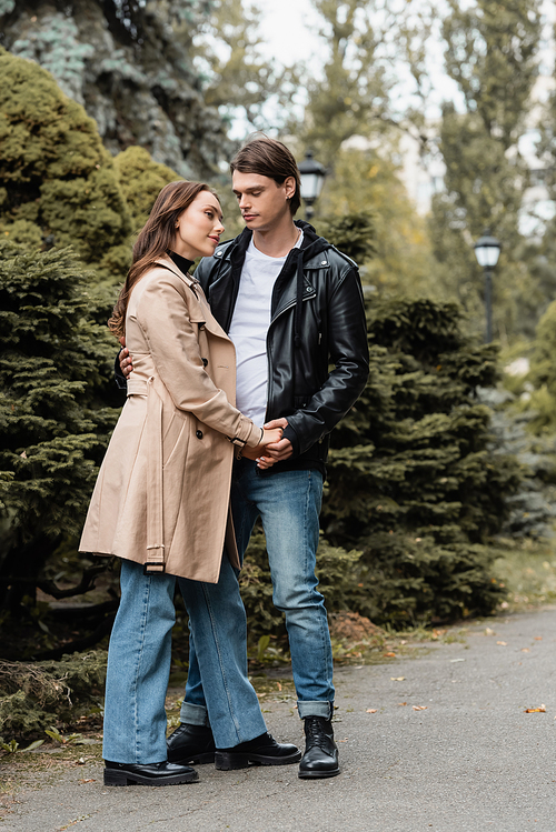 full length of young man and pleased woman holding hands in autumnal park