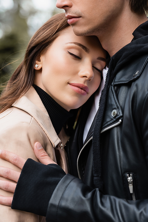 pretty young woman with closed eyes leaning on chest of boyfriend in black jacket