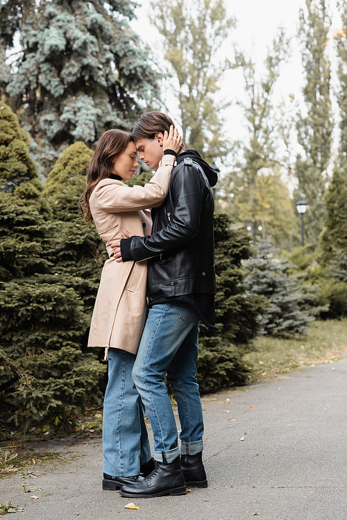 full length of young woman in beige trench coat hugging boyfriend in black jacket