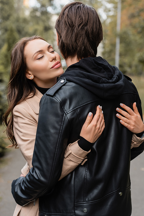 young and pretty woman in coat hugging boyfriend in black jacket