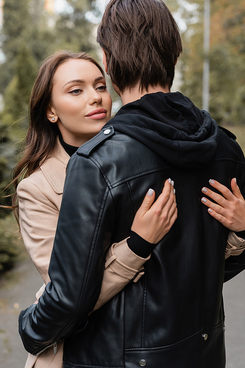 young and pretty woman in beige coat hugging boyfriend in black jacket