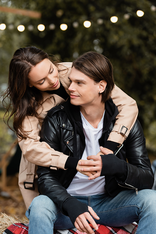 smiling young woman in trench coat hugging stylish boyfriend in park