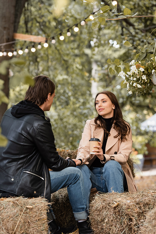 young and pretty woman with paper cup holding hands with boyfriend in autumnal park