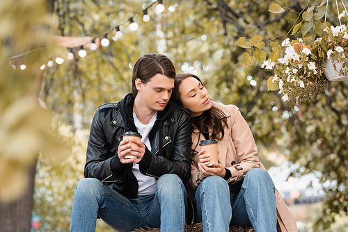 young woman with closed eyes holding paper cup and leaning on shoulder of boyfriend