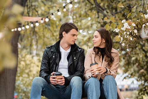 young woman and man in stylish outfits holding paper cups and looking at each other