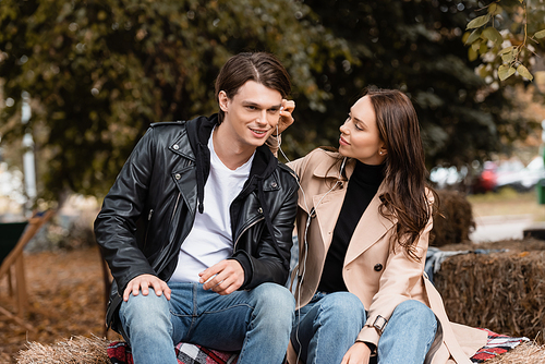 smiling young woman adjusting wired earphone in ear of happy boyfriend