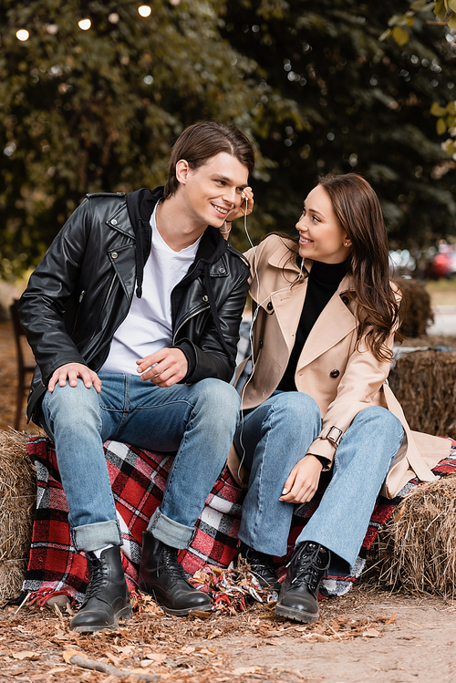 cheerful young woman adjusting wired earphone in ear of happy boyfriend