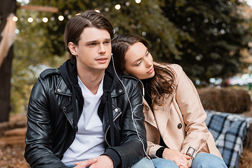 young woman and man sharing wired earphones while listening music together in park