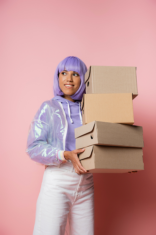 happy african american woman in purple wig holding carton boxes on pink