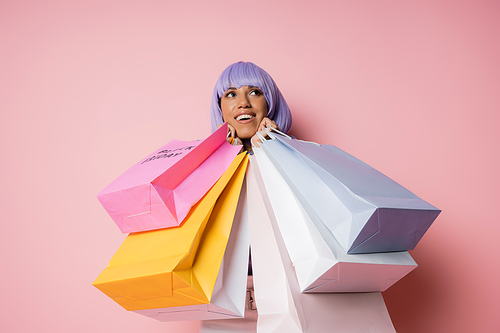 amazed african american woman with purple hair holding shopping bags with black friday lettering on pink