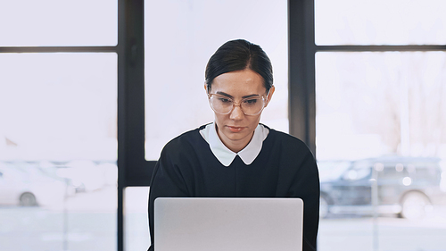 focused businesswoman in eyeglasses working on laptop in office