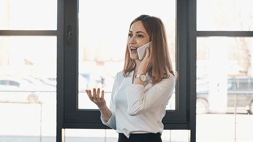 excited businesswoman gesturing during conversation on smartphone in office
