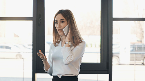 shocked woman talking on mobile phone and gesturing in office