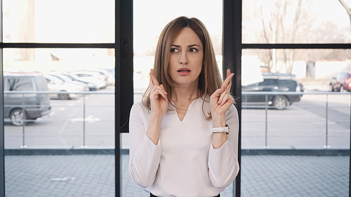 worried woman holding crossed fingers before job interview in office