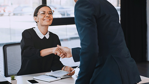 smiling businesswoman holding resume and shaking hands with man after job interview