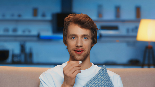 positive young man holding popcorn while watching comedy movie in living room