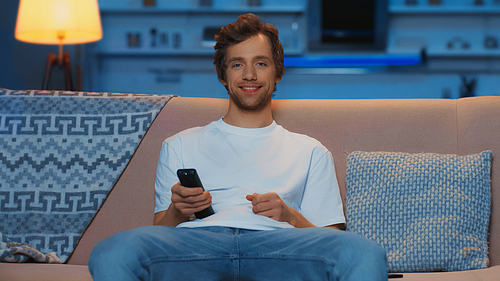 happy young man using remote controller while watching tv on couch