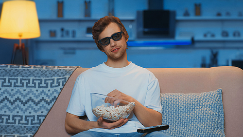 pleased man in 3d glasses holding bowl with popcorn while watching movie in living room