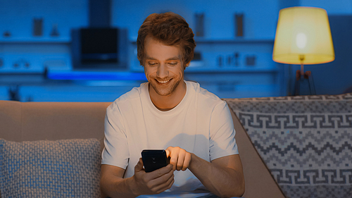 happy young man smiling while chatting on smartphone in evening