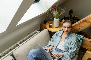 High angle view of woman looking at camera near laptop on couch in living room