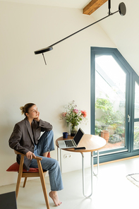 Freelancer in jacket sitting near gadgets and cup at home