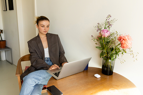 Young woman using laptop near smartphone and flowers at home
