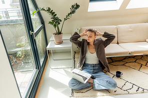 Woman in jacket looking at laptop near cup on carpet at home