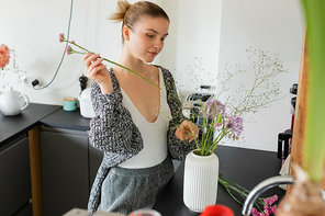 Woman in warm cardigan making floral bouquet in vase at home