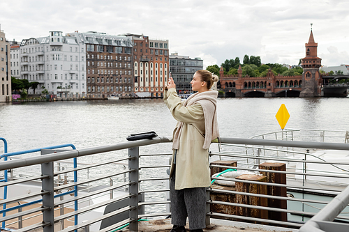 Side view of young woman taking photo on pier in Berlin