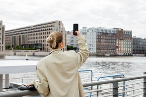 Back view of woman in trench coat taking photo on cellphone in Berlin