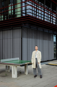 Stylish woman in trench coat standing near ping-pong table outdoors in Berlin