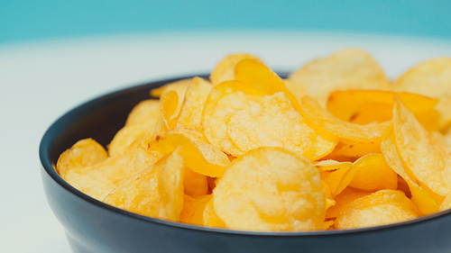 close up view of crispy and ridged potato chips in bowl on blue