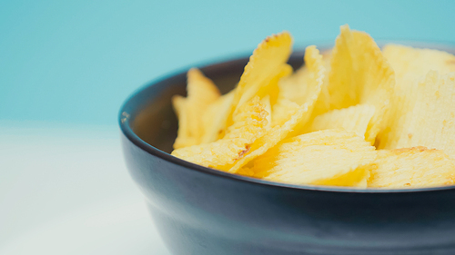 close up view of crunchy and ridged potato chips in bowl on blue with copy space