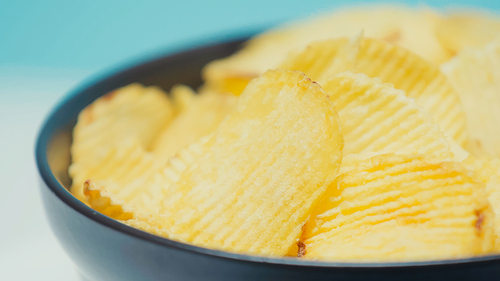close up view of crunchy and rippled potato chips in bowl on blue