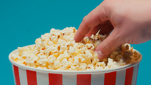 cropped view of man taking popcorn from big paper bucket isolated on blue