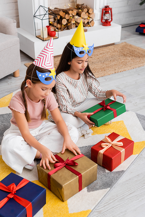 High angle view of preteen girls in party caps and masks looking at presents during birthday at home