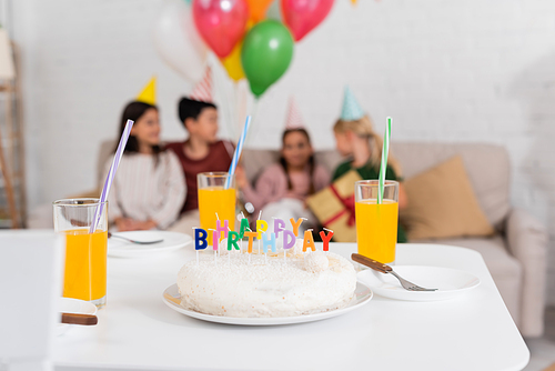 Birthday cake and orange juice on table near blurred kids at home