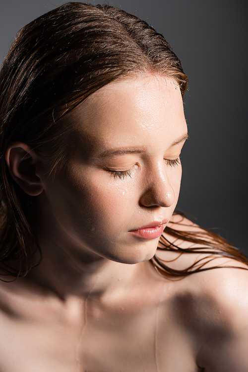 Young model with wet hair and naked shoulder closing eyes isolated on grey