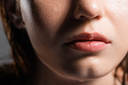 Cropped view of water drops on lips of young woman isolated on grey