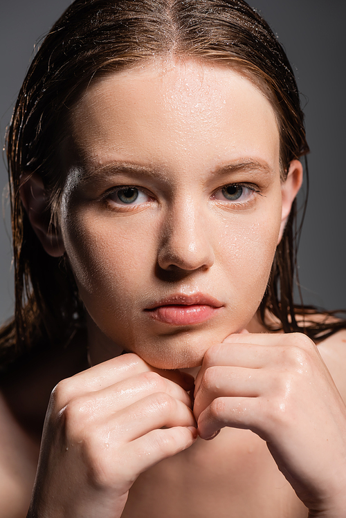 Portrait of pretty young woman with wet skin touching chin isolated on grey