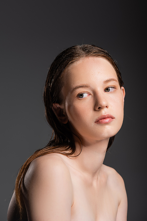 Young woman with wet hair and naked shoulders looking away isolated on grey