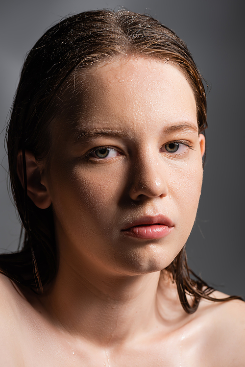 Fair haired model with naked shoulders and wet skin looking at camera isolated on grey