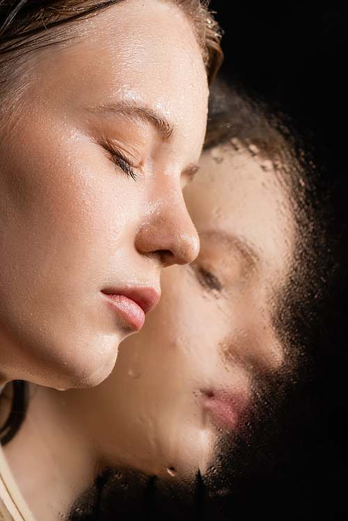 Close up view of young woman with wet skin posing near near mirror on black background